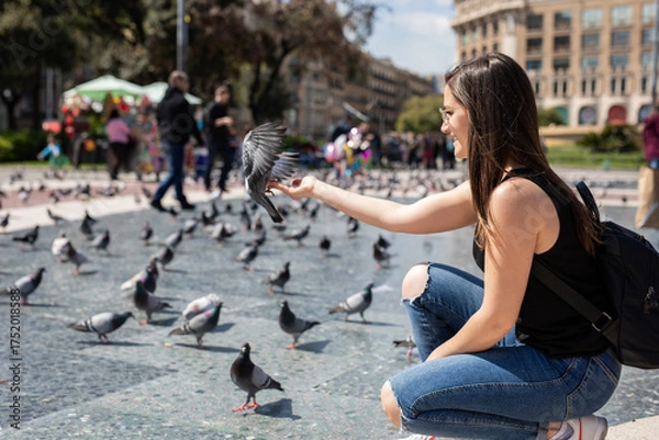 Obraz Cheerful young woman in Barcelona feeding pigeons in a city square, enjoying a beautiful sunny day and creating a lasting memory on her European vacation, travel adventure