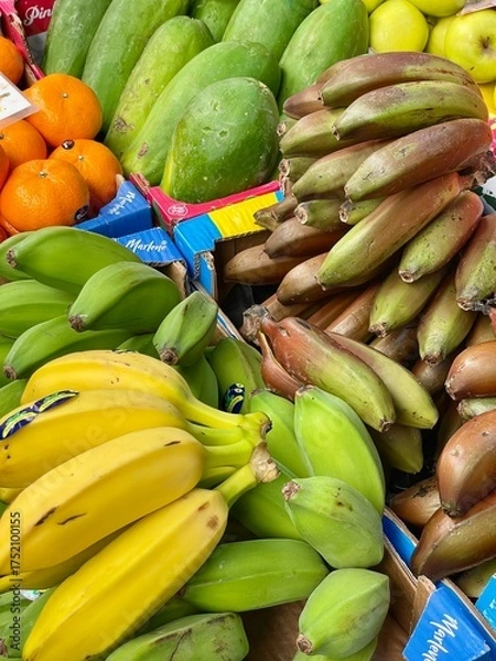 Fototapeta Assorted tropical fruits including various bananas and papayas on a market stall. Colorful, fresh, and organic produce for healthy eating and exotic food themes.