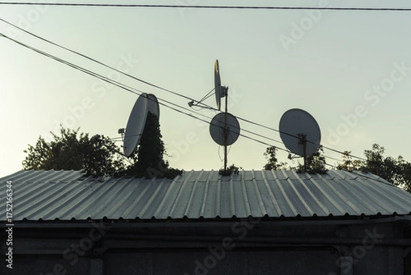 Obraz several parabolic antennas on a small gray roof