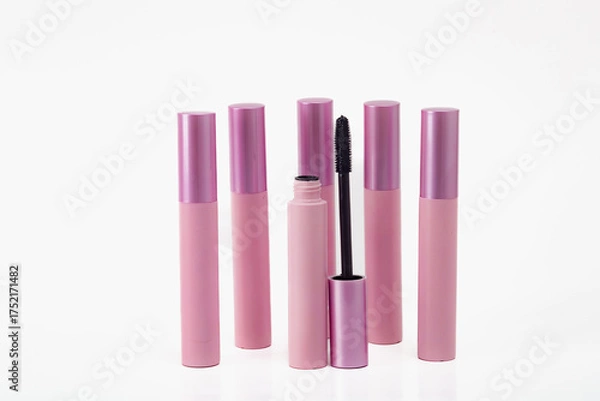 Fototapeta A row of six pink mascara tubes with a black brush in the middle. The tubes are lined up next to each other on a white background.