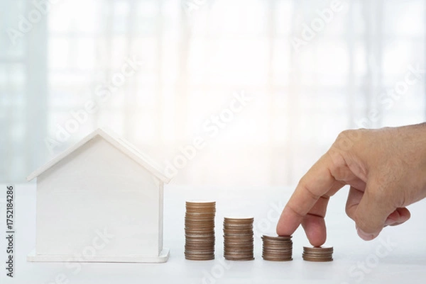 Fototapeta White house and man's fingers walking up the stairs, stacked coins and beautiful blurred background. Home loan concept, real estate business.