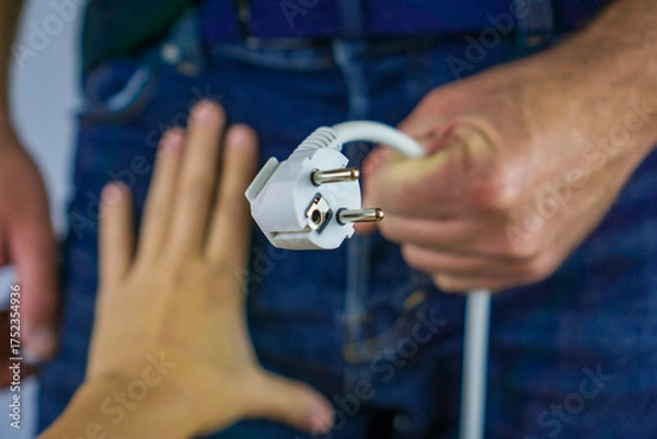 Obraz male hand holding a white european power plug extended toward a second outstretched hand against a man in blue jeans concept of male sexual health, energy transfer and connection, erectile dysfunction