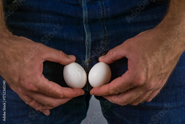 Obraz male vasectomy and reproductive health, showing a man holding two eggs near jeans to represent fertility and sterilization.