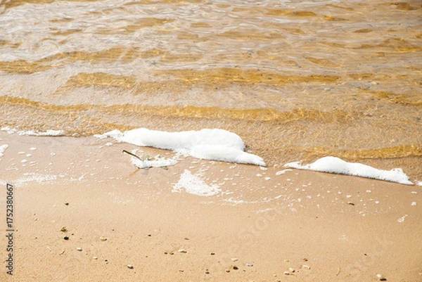 Fototapeta Polluted water with foam and debris flows next to muddy banks, showing environmental degradation. The murky liquid and dirty surroundings highlight the impact of contamination