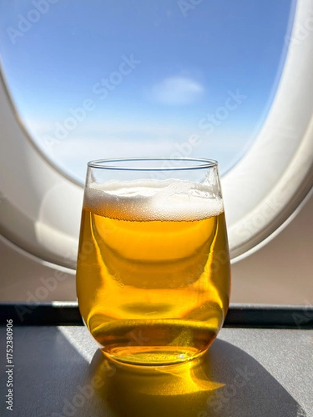 Obraz Close up view of a glass of lager beer in front of the window of a business class cabin of a passenger plane. no people.