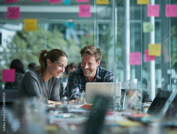 Fototapeta Colleagues collaborate happily on laptop in modern office with colorful notes
