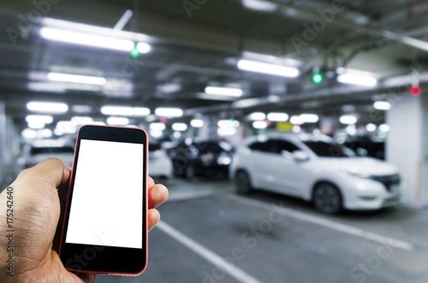 Fototapeta hand using mobile smart phone with blurred image of indoor car parking garage area, RFID solution management system, internet, social media and car parking sensor technology concept