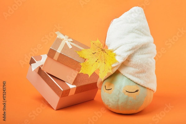 Fototapeta A pumpkin smeared with clay with a towel on top and gift boxes on an orange background, the time for holiday gifts and sales concept