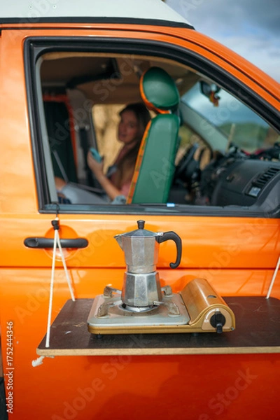 Fototapeta Coffee pot on portable stove attached to orange camper van door.