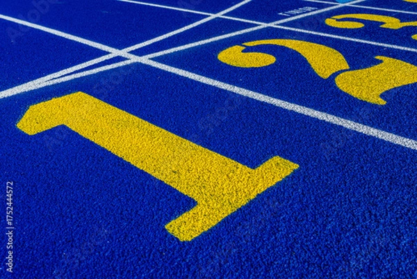 Obraz Close up photo of outdoor running track lane yellow number one, 1, on a new blue track with white lane lines.