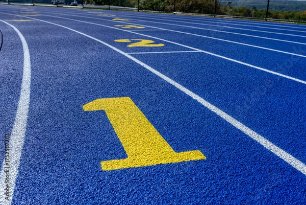 Obraz Close up photo of outdoor running track lane yellow number one, 1, on a new blue track with white lane lines.