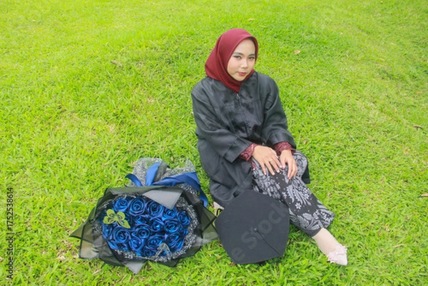 Fototapeta Beautiful Indonesian Muslim woman with a happy smiling expression sitting on the green grass