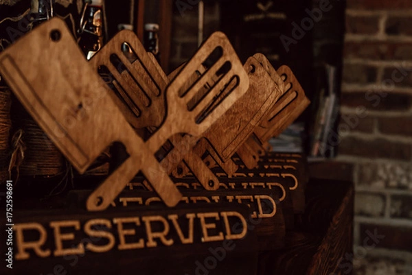 Fototapeta in warm restaurant atmosphere, wooden reserved signs shaped like spatulas and forks are lined up on shelf, creating unique and inviting dining experience for guests. close up.