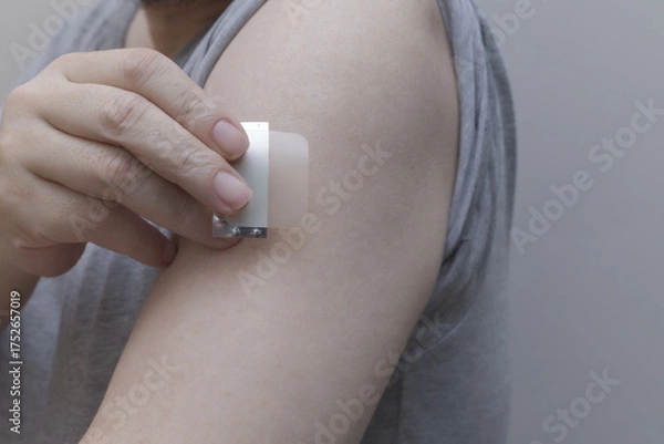 Fototapeta A close-up of a hand applying a nicotine patch to the upper arm. Represents Nicotine Replacement Therapy (NRT) and the user's commitment to quit smoking and pursue better health