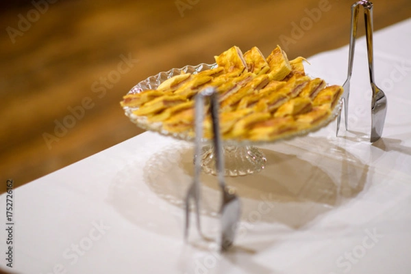 Fototapeta Delicious Homemade Apple Tart Baked Golden Brown Served Freshly Cut on a Clear Glass Cake Stand Ready for Guests to Enjoy at a Festive Gathering