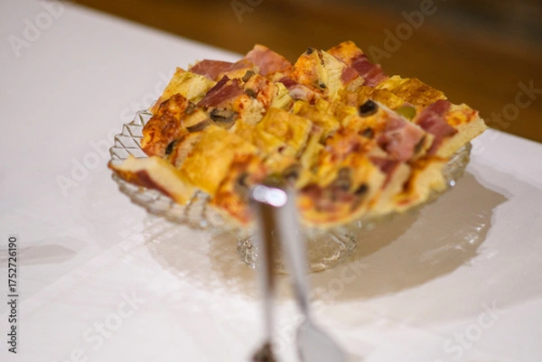 Fototapeta Delicious savory pie sliced on a glass plate with a fork about to take a piece presented on a white tablecloth for a delightful meal or party celebration