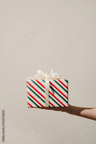 Fototapeta A single wrapped Christmas present with ribbons held in one hand