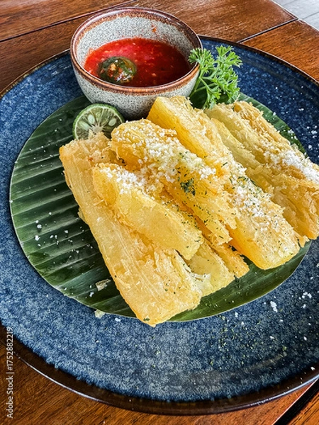 Fototapeta Crispy fried cassava served with spicy sambal and lime on a black plate, a traditional Indonesian snack with delicious flavor and texture.