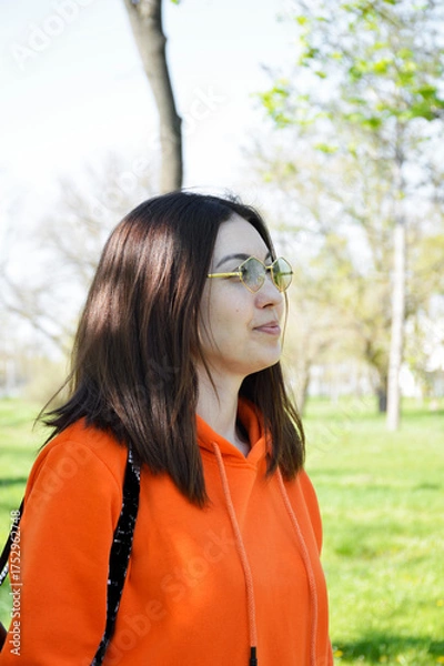 Fototapeta A beautiful woman with a bob haircut and sunglasses takes a walk in a city park. Strolling in the fresh air. The beautiful girl poses. Slanted eyes.