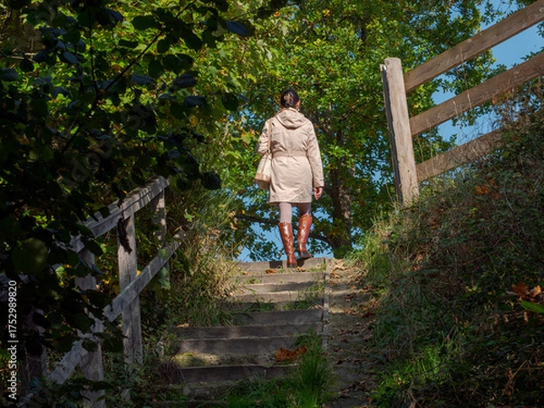 Obraz Clecy, Normandy, October 4, 2025. Autumn walk on forest steps. A woman in a coat and leather boots walks up forest steps in an autumnal setting. A charming scene depicting the tranquility of nature