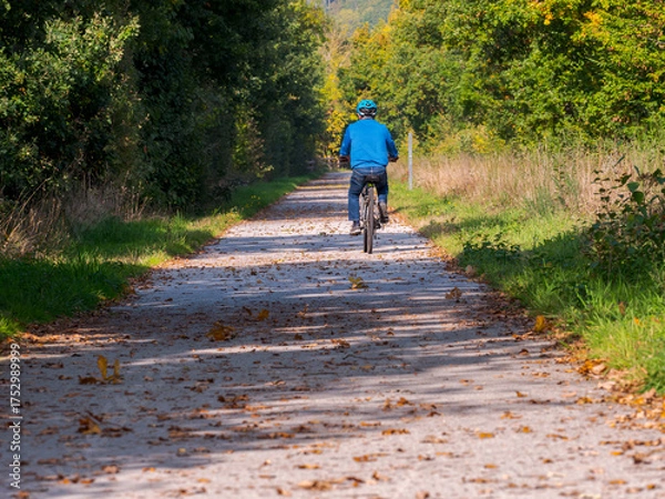 Fototapeta Clecy, Normandy, October 4, 2025. Autumn bike ride on a forest path. A man rides his bike on a quiet country path surrounded by trees in autumn colors