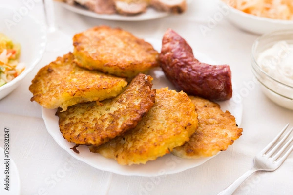 Fototapeta Potato pancakes with fried sausage on white plate
