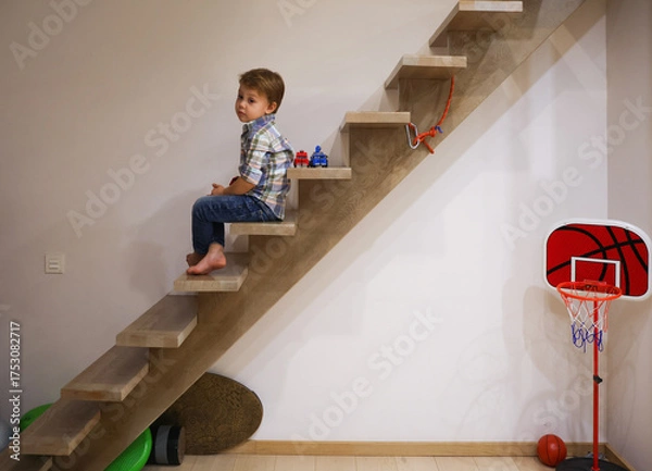Fototapeta little three-year-old boy sits alone and sadly on the stairs of his house