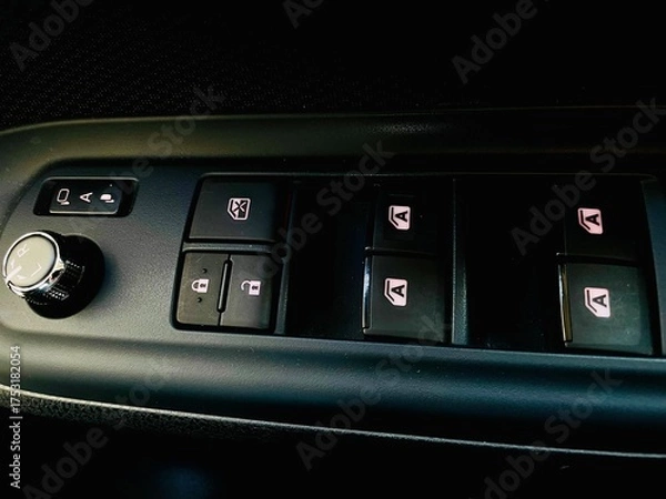 Fototapeta A close-up view of a vehicle's driver-side control panel, featuring power window switches, door lock/unlock buttons, a window lock button, and a knob for adjusting the side mirrors.