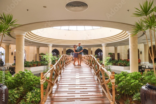 Fototapeta Loving adults stand hugging decorative bridge inside a building.