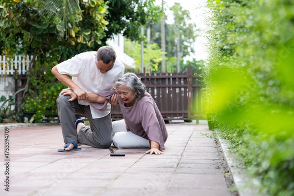 Fototapeta An elderly woman sits on the ground after a fall, assisted by a concerned older man in a quiet outdoor setting. The scene highlights senior vulnerability, caregiving, and the importance of safety.