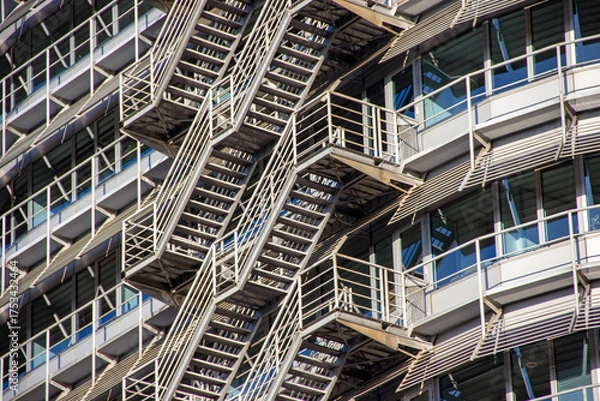 Obraz Modern architectural design featuring metallic fire escape stairs attached to a contemporary building with large glass windows showcasing urban living and safety features