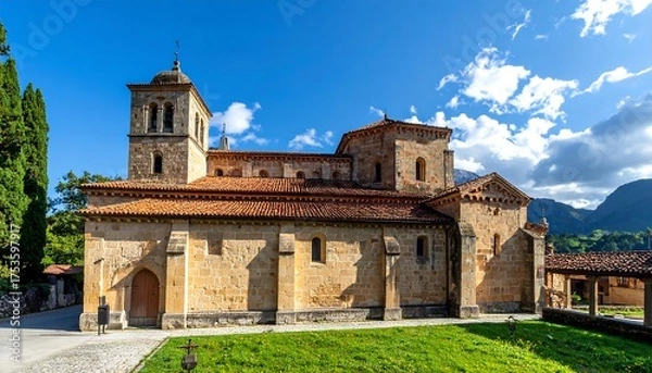 Obraz A stone church with a tower and red tile roof under a clear, bright blue sky. It sits on a green lawn with nearby mountains