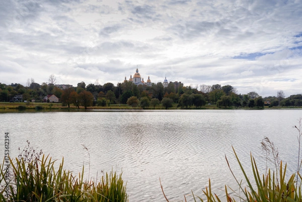 Fototapeta The church is located among the trees. In front of it is a lake. Landscape.