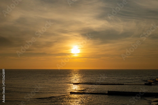 Fototapeta Sunrise over calm sea with breakwaters and golden sky reflection. Landscape photography with copy space. Summer morning and travel concept