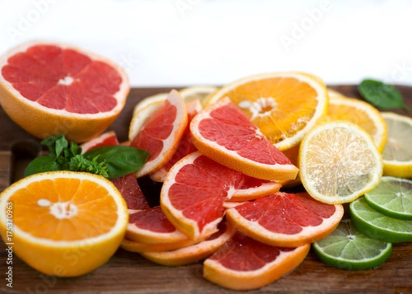 Fototapeta sliced citrus decorated with basil on wooden and white backgrounds. Orange, grapefruit, lime, lemon.