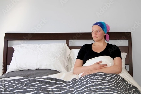 Fototapeta Young cancer patient in a headscarf looks out the window while resting in bed