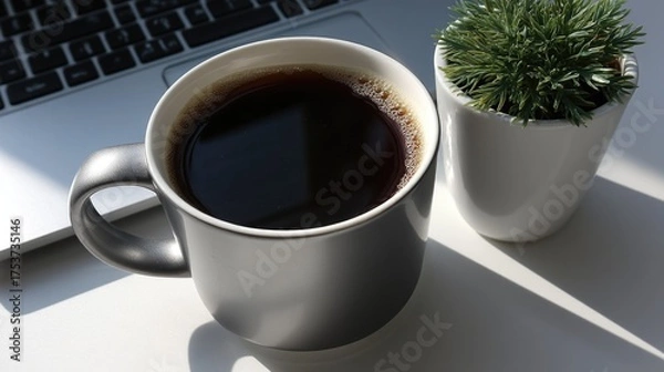 Fototapeta Black coffee in gray mug next to green plant and open laptop on sunny desk