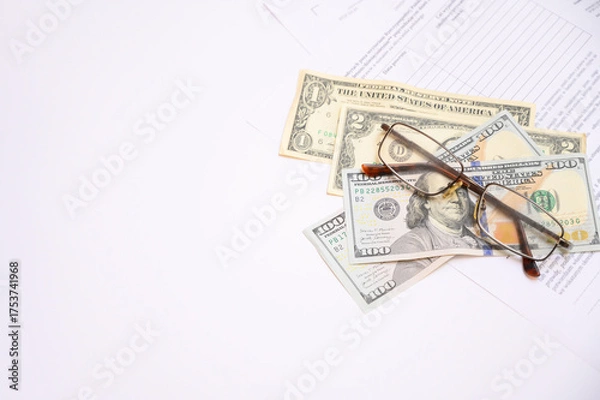 Fototapeta Close-up image showing US dollar banknotes, eyeglasses and financial documents on a white background. Concept of accounting, finance, business analysis, investment and personal budget planning.