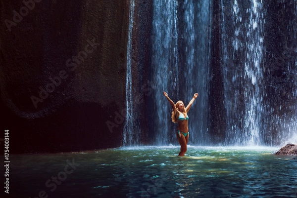 Obraz Woman stand in underground cave pool under falling fresh water of Tukad Cepung waterfall. Nature day tour, hiking activity adventure and fun at family tourist camp on summer vacation in Bali island