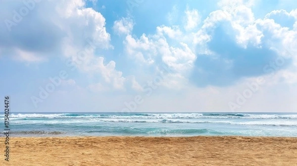 Fototapeta A beautiful beach scene with sandy shores leading into calm ocean waters and gentle waves under a bright blue sky filled