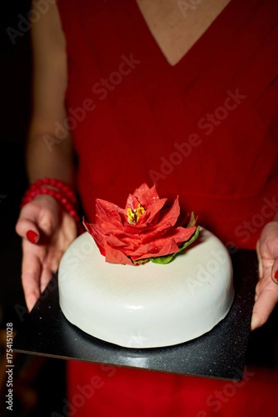 Obraz The woman presents an elegantly crafted cake featuring a vibrant flower on top. The surroundings are softly lit, enhancing the festive atmosphere of the occasion.