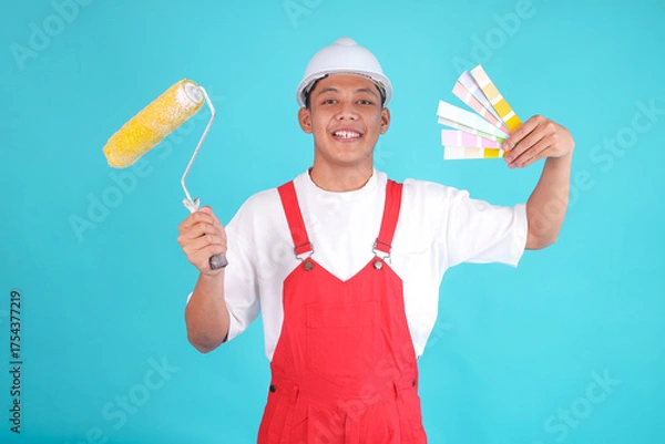 Obraz Smiling Painter Man in Red Overalls Holds Paint Roller and Color Swatches, Ready for Project