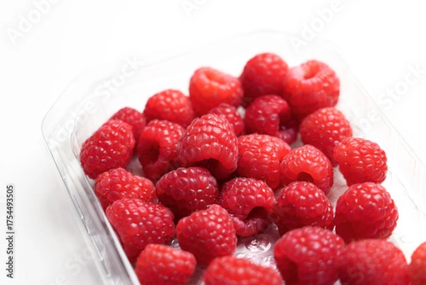 Fototapeta Fresh raspberries in plastic packaging on a white table