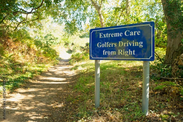 Obraz Warning of golfers at the tee seen on a rural country path which is about to exit near the golf tee at an English country club. The tee is just beyond the hedge on the right.