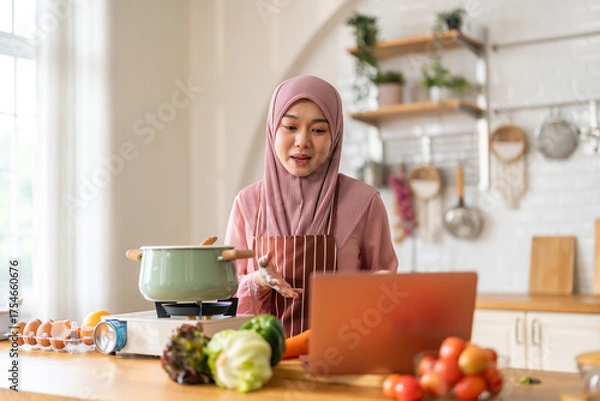 Fototapeta Muslim woman vlogger live streaming cooking online in kitchen look at camera with vegetables, content creator culinary class at home studio, halal food influencer cooking live, video for social media