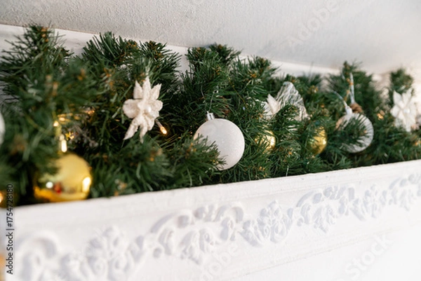 Fototapeta Christmas garland of green fir with gold and white balls on the fireplace in the bright living room