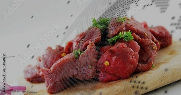 Obraz Lying raw beef chunks on wooden cutting board in kitchen with parsley, cracked pepper, onion slices