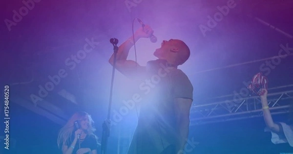 Fototapeta Gripping microphone singer belting out song on stage, with red maracas and colored LED lights