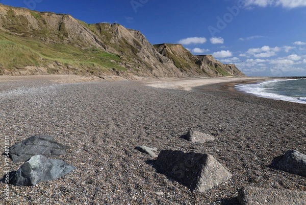 Fototapeta Landscape photo with a view of the North Sea coast, beach with large stones and rocks in the background against a blue sky with clouds near Bovbjerg Lighthouse in Lemvig, Denmark