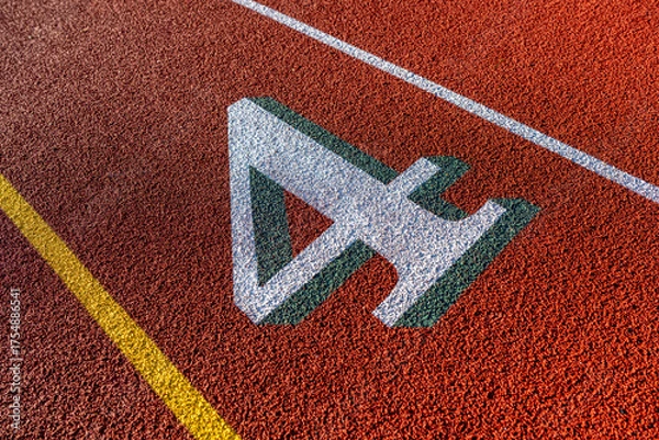 Fototapeta Close up photo of outdoor running track lane white number four, 4, with green shadow, on a new red track with white lane lines.